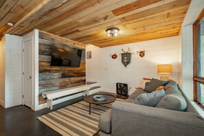 Een gezellige woonkamer met een televisie, een bankje, een bank en een ventilator.