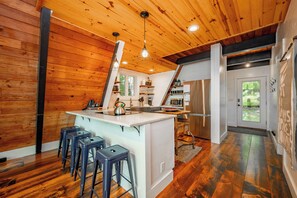 A kitchen with wooden walls, a central island with stools, stainless steel appliances, and pendant lighting.