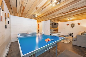 A ping pong table with paddles, a sofa, and a television in a room with wooden walls and ceiling.