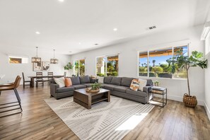 Un salon spacieux avec un canapé d’angle, une table basse et un coin repas avec des chaises.