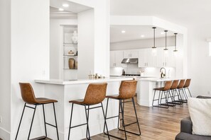 A modern kitchen with white cabinetry, a central island with bar stools, and pendant lighting.