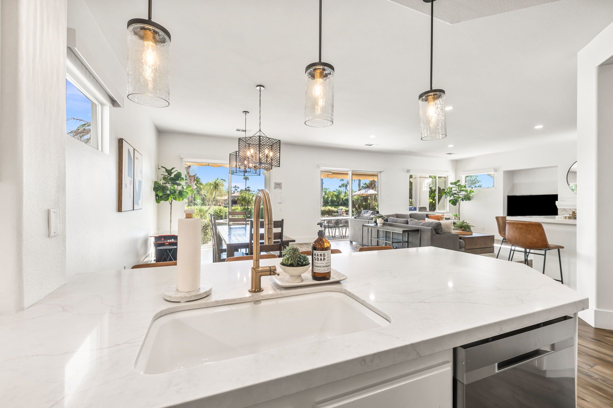 A modern kitchen with a large island, pendant lights, and a view of the outdoors.