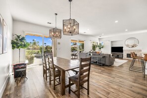 A spacious living area with a dining table, chairs, a kitchen, and a large TV.