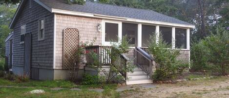 A small, single-story house with a porch, a small staircase, and a fenced yard.