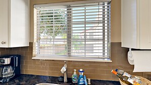 A kitchen with a double sink, a coffee maker, and a window with blinds.