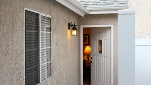 A house exterior with a textured stucco wall, a window with blinds, a door, and a wall-mounted light fixture.