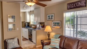 A compact living space with a kitchenette, a brown leather couch, a lamp, and a 'WELCOME' sign.