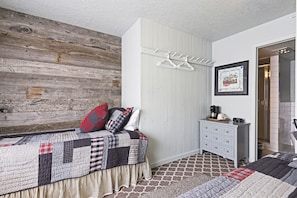 A bedroom with a wooden wall, a bed with a quilt, a dresser, and a framed picture on the wall.
