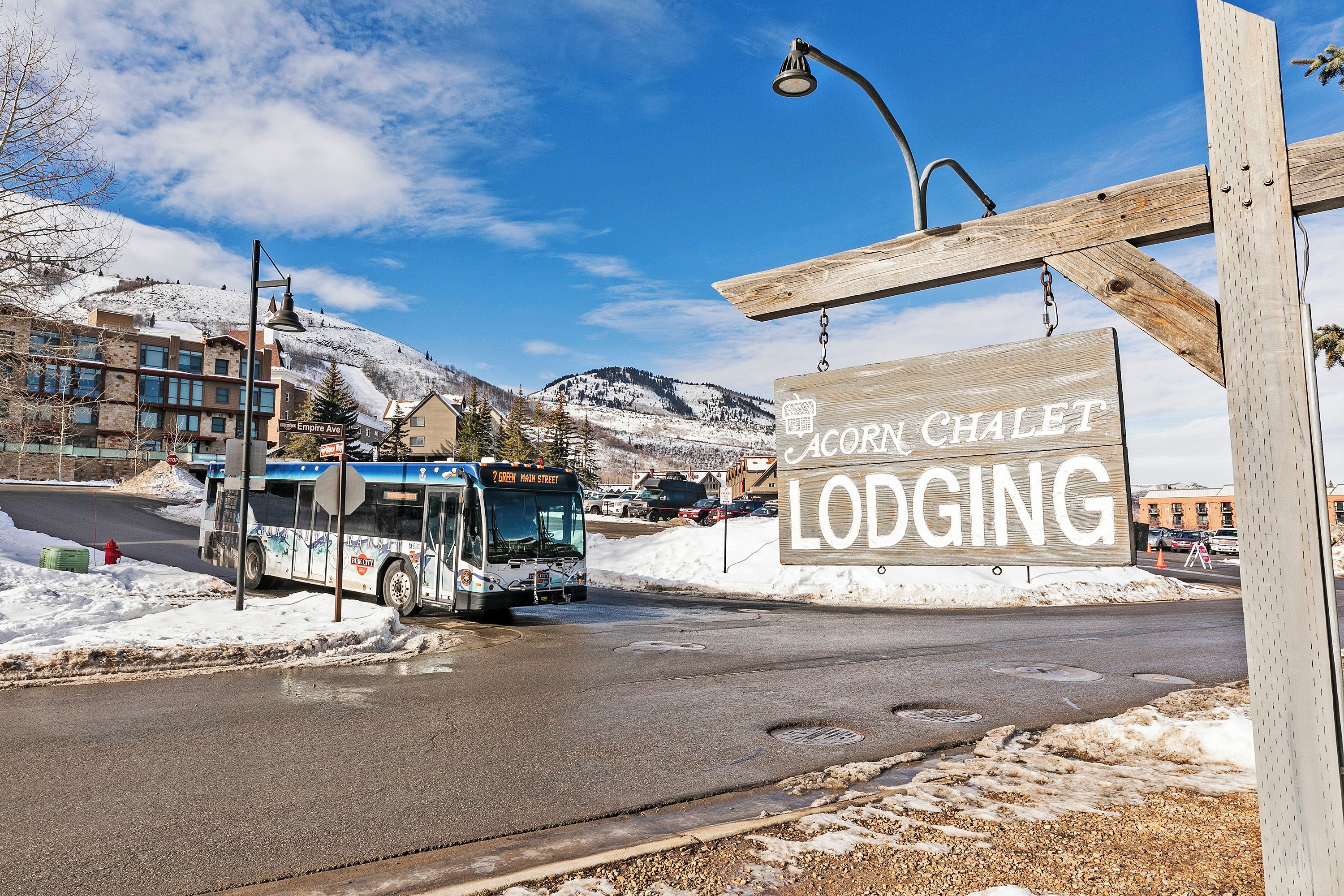 En buss vid ett busshållplats med en skylt som visar vägen till ”Acorn Chalet Lodging” i bakgrunden.
