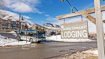 En buss vid ett busshållplats med en skylt som visar vägen till ”Acorn Chalet Lodging” i bakgrunden.