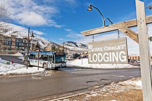 A bus at a stop with a sign for 'Acorn Chalet Lodging' in the background. - Acorn Chalet Studio | 100 Yards to Park City Mountain | Sleeps 2 (Park City)