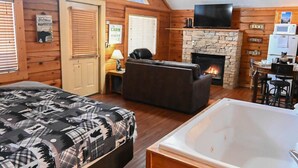 Een gezellig chaletinterieur met een open haard, een bank, een bed, een badkuip en een televisie.