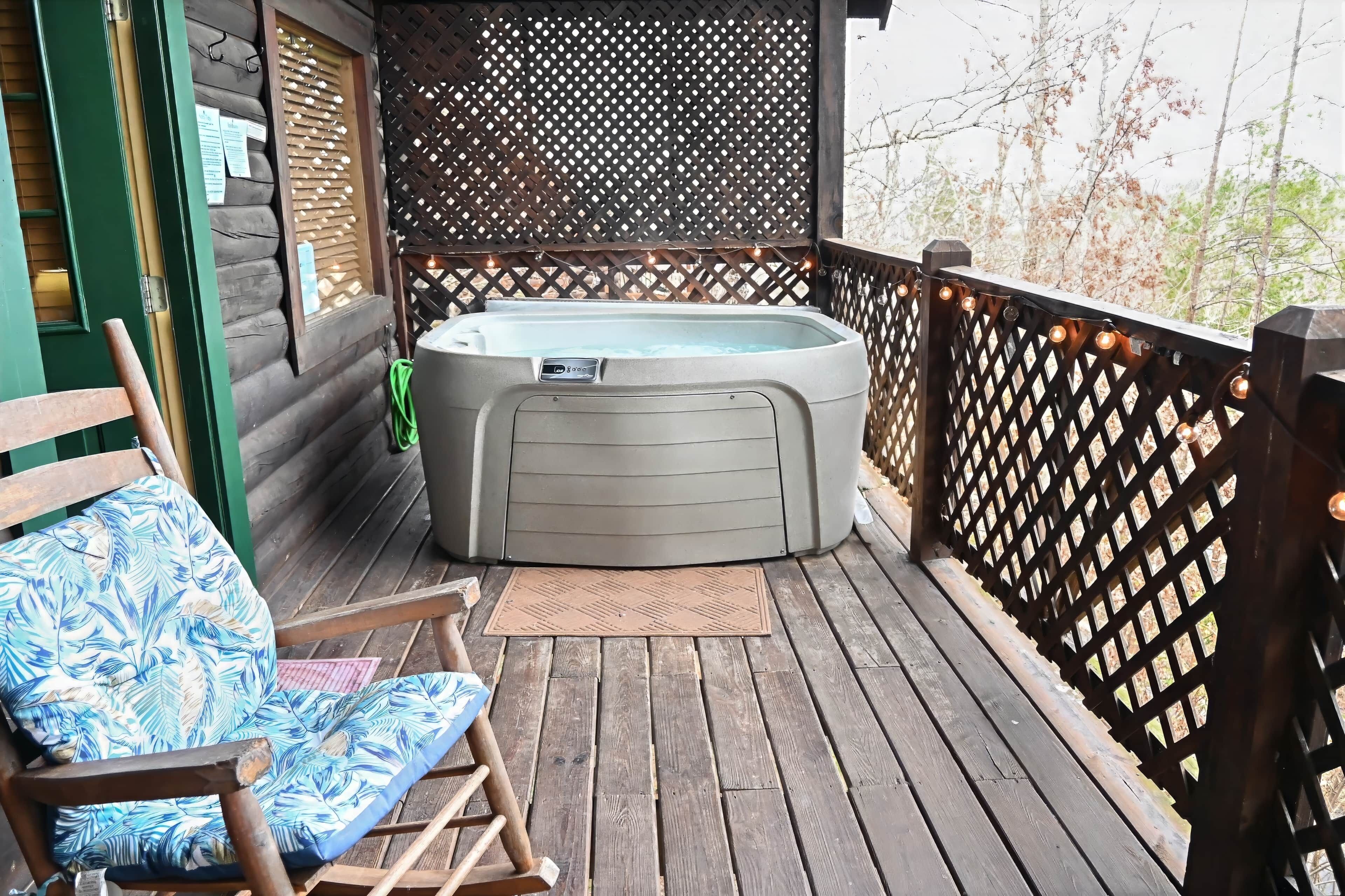 Eine Holzterrasse mit Whirlpool, einem Schaukelstuhl und einem Holzzaun mit Lichterketten.