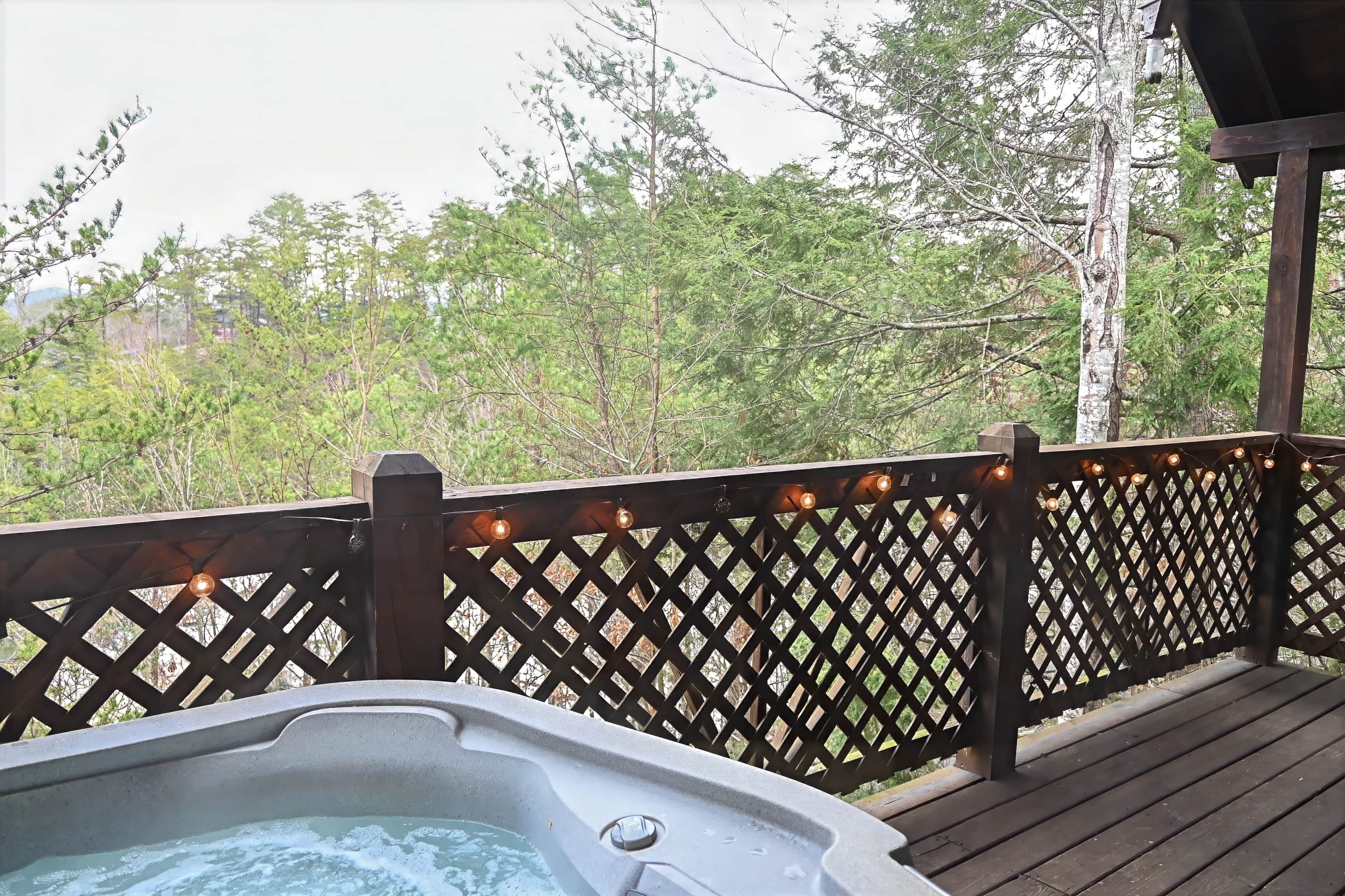 A hot tub on a wooden deck with a lattice railing and string lights.