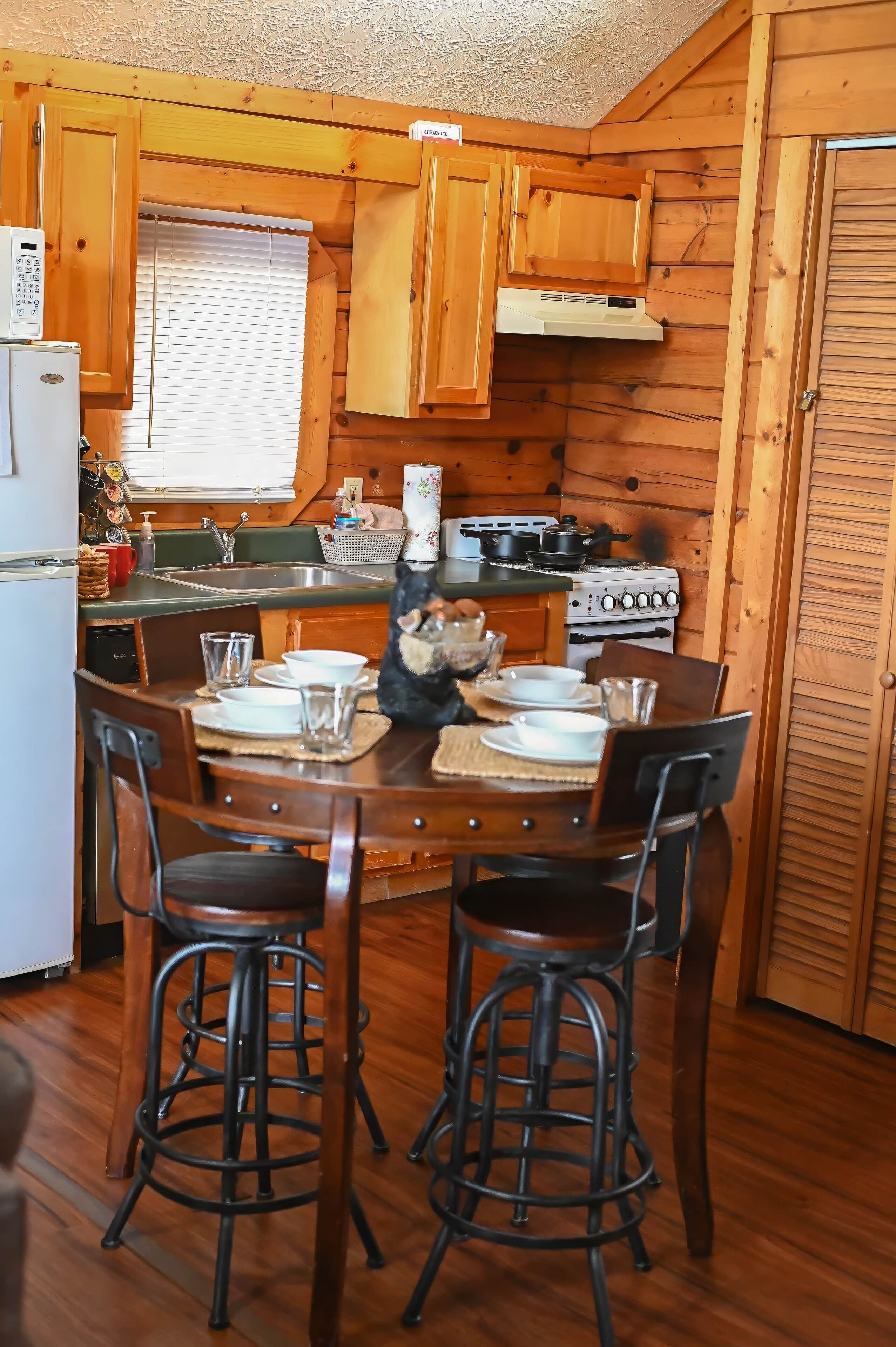 Una cocina de cabaña de madera con una mesa de comedor, taburetes de bar, un refrigerador, una estufa y un lavabo.