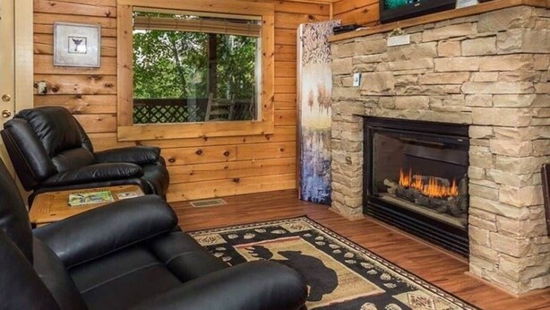 Een gezellig interieur van een blokhut met een stenen open haard, een leren fauteuil en een televisie erboven.
