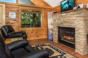 Een gezellig interieur van een blokhut met een stenen open haard, een leren fauteuil en een televisie erboven.