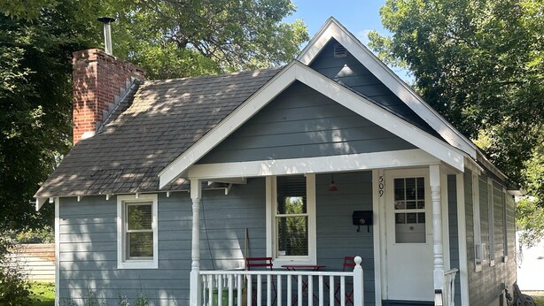 A small, single-story house with a gabled roof, a front porch with a white railing, and a number '509' on the door. - Exquisite 1-Bedroom House on North Church Ave (Bozeman)