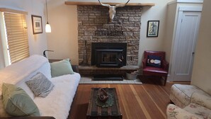 A cozy living room with a stone fireplace, a sofa, a red chair, and a wooden coffee table. - Exquisite 1-Bedroom House on North Church Ave (Bozeman)