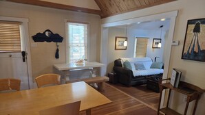A cozy living room with a wooden floor, a sofa, a dining table with chairs, and a bench. - Exquisite 1-Bedroom House on North Church Ave (Bozeman)