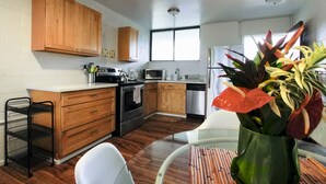 Cocina compacta con armarios de madera, un microondas, una tetera y un refrigerador.