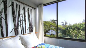 Habitación de hotel con un ventanal grande, una cama con almohadas blancas, una colcha azul y blanca a rayas y una pared con diseño de bambú.