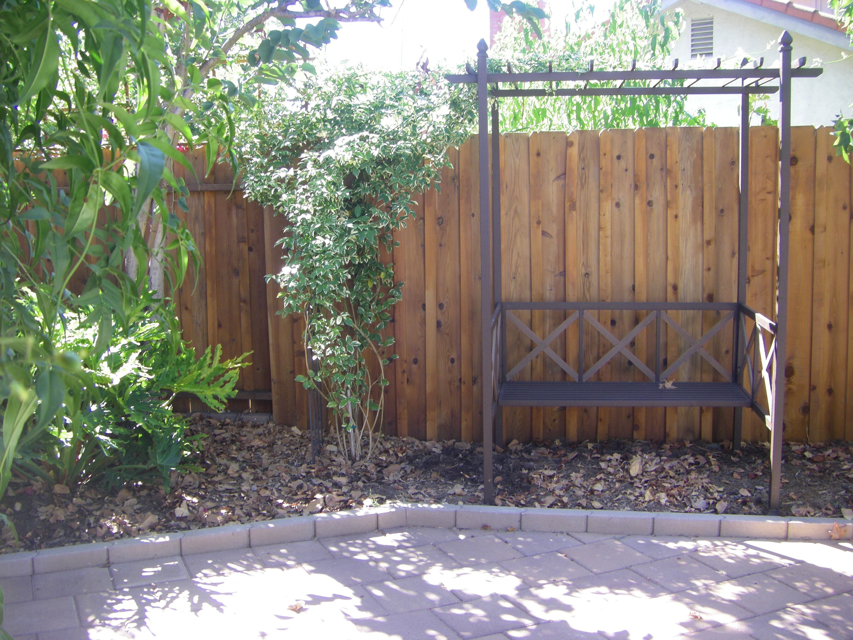 A wooden fence, a metal bench, and a garden bed with mulch.