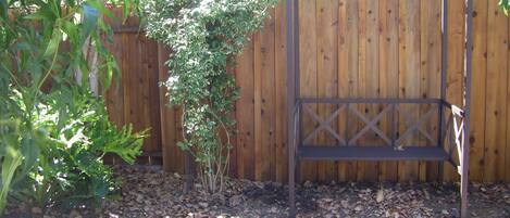 A wooden fence, a metal bench, and a garden bed with mulch.