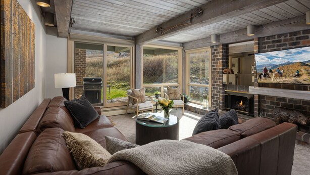 A modern living room with a leather sofa, a fireplace, and large windows offering a view of the outdoors.