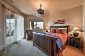 Ein Schlafzimmer mit einem Bett, Nachttischen, einem Sessel, einem Fenster und einem Deckenventilator.