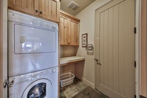 A laundry room with stacked washers and dryers, wooden cabinets, a basket, and a door with a lock. - Private Desert Sunset Getaway (Santa Clara)