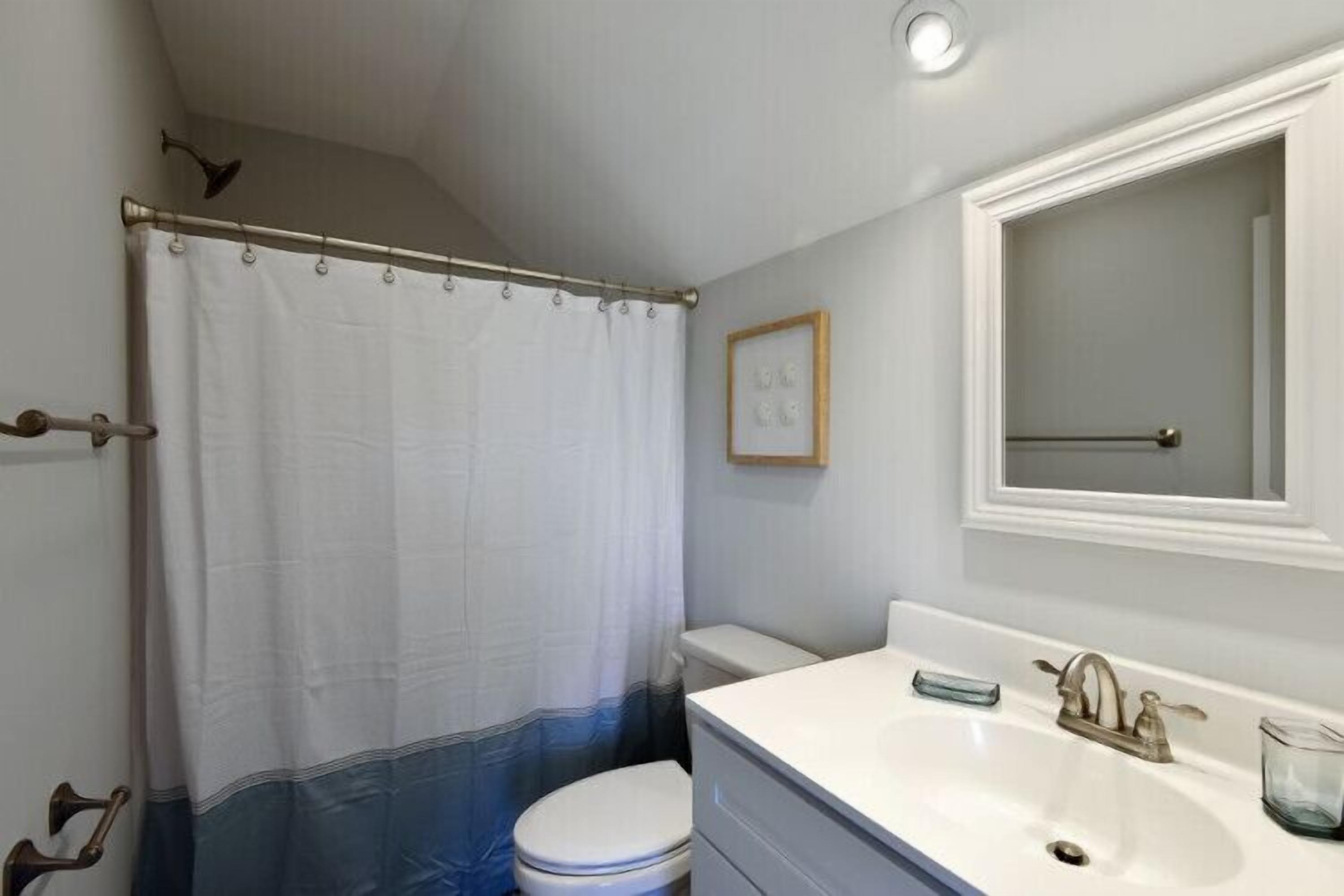 A bathroom with a shower curtain, toilet, sink, and mirror.