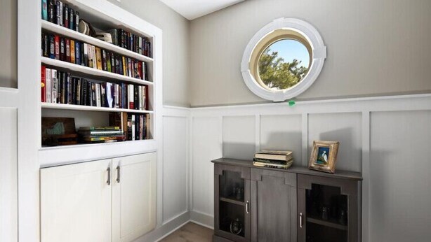 A room with a built-in bookshelf, a small cabinet with glass doors, and a round window with a view of trees. - Updated and Modern Corolla Beach Retreat! (Corolla)