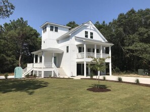 A two-story white house with a front porch and a small tree in the front yard.