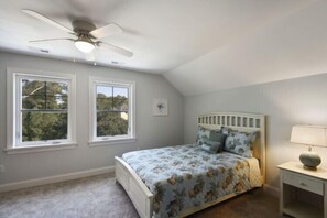 A bedroom with a bed, two windows, a ceiling fan, and a bedside table with a lamp.
