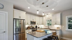 A modern kitchen with white cabinetry, stainless steel appliances, and a central island with stools. - Updated and Modern Corolla Beach Retreat! (Corolla)