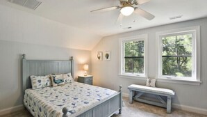 A bedroom with a bed, a bench, a ceiling fan, and windows. - Updated and Modern Corolla Beach Retreat! (Corolla)