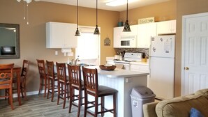 A kitchen with a central island, wooden chairs, a dining table, and a trash bin.