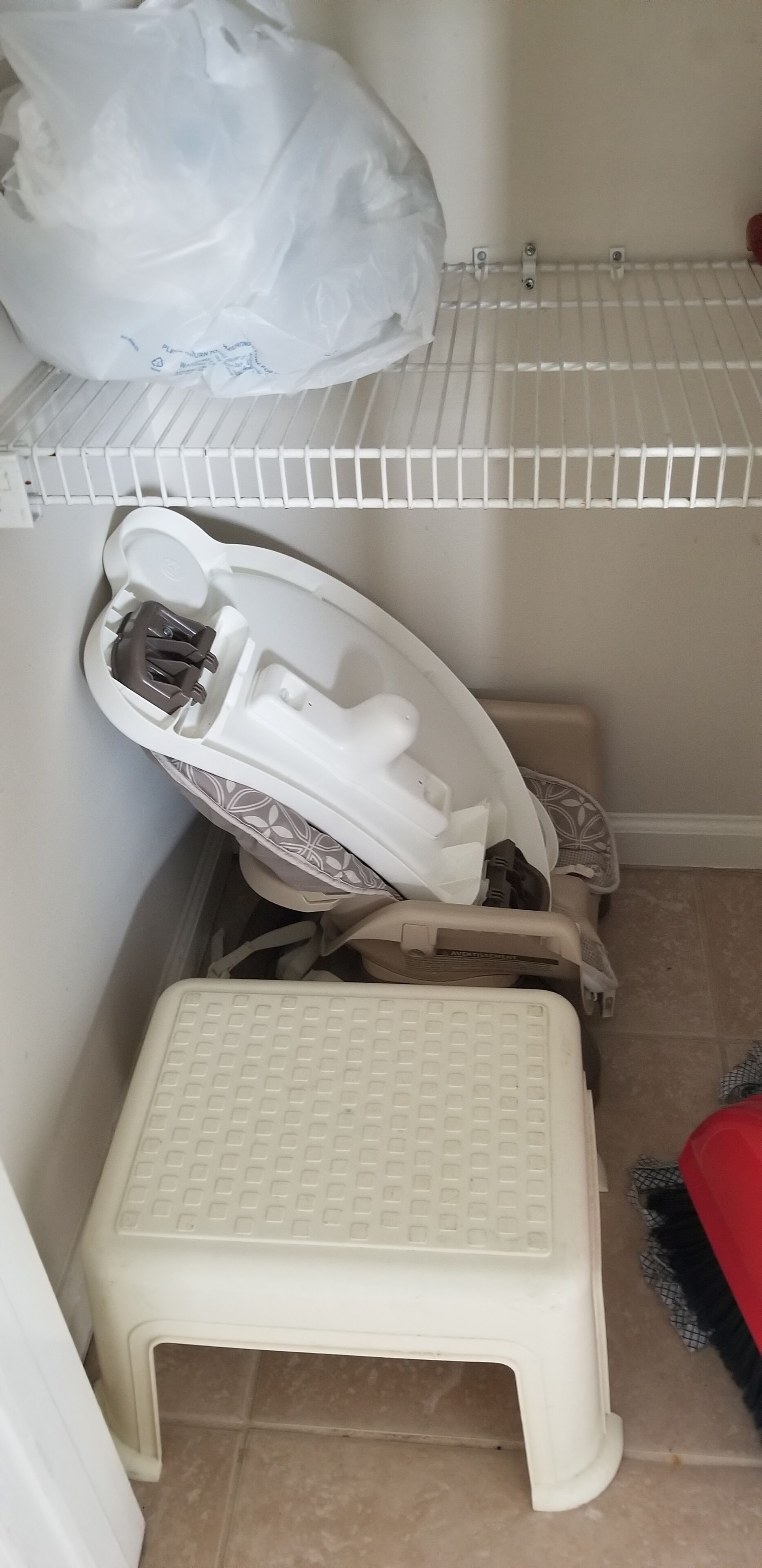 A corner of a room with a white plastic stool, a white shelf, and a white plastic bag.