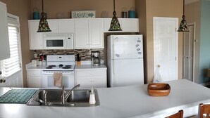 A kitchen with white cabinets, a microwave, a stove, a refrigerator, a sink, and a dining area with chairs.