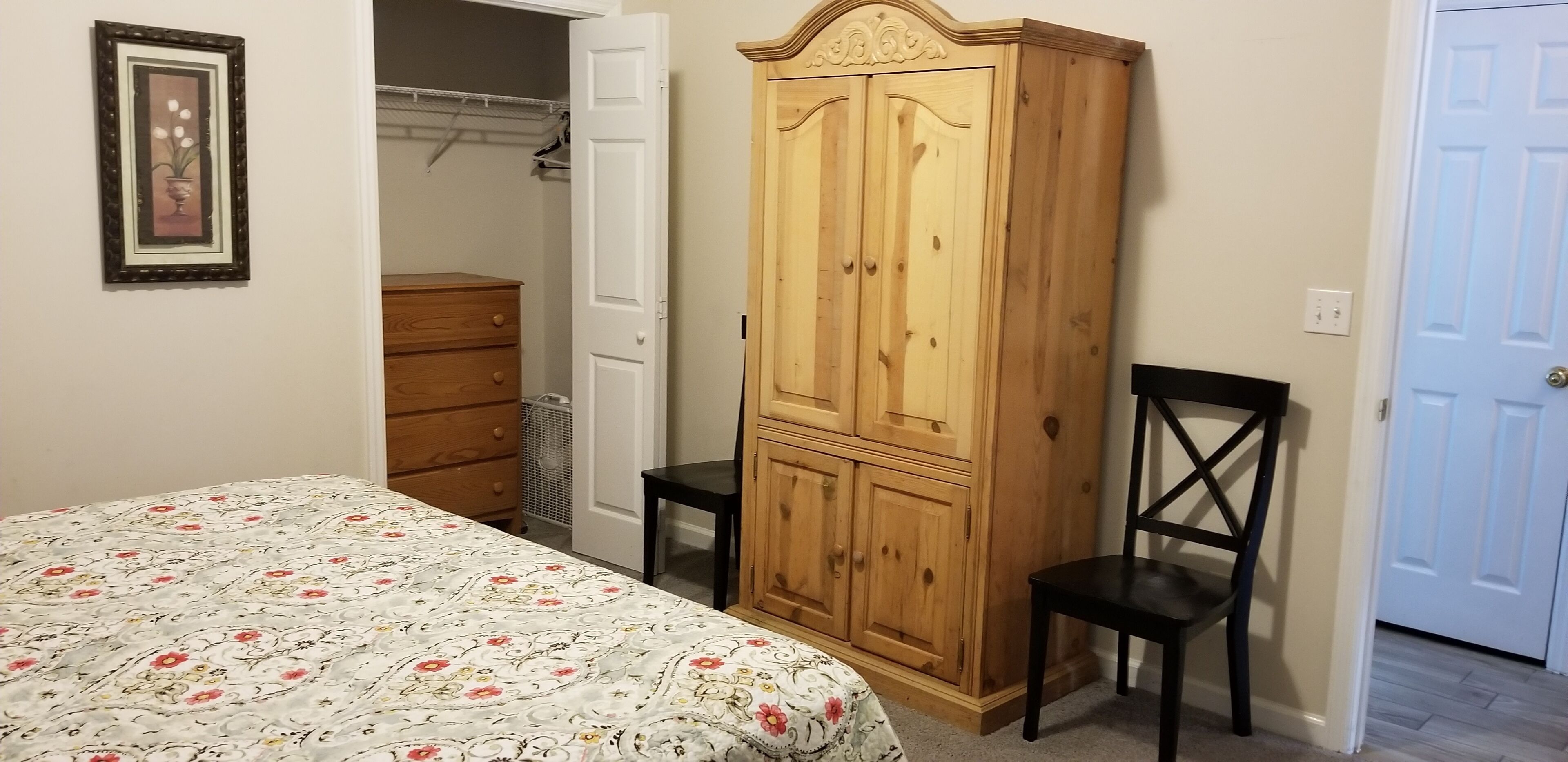 Un dormitorio con cama, armario de madera, silla y puerta.