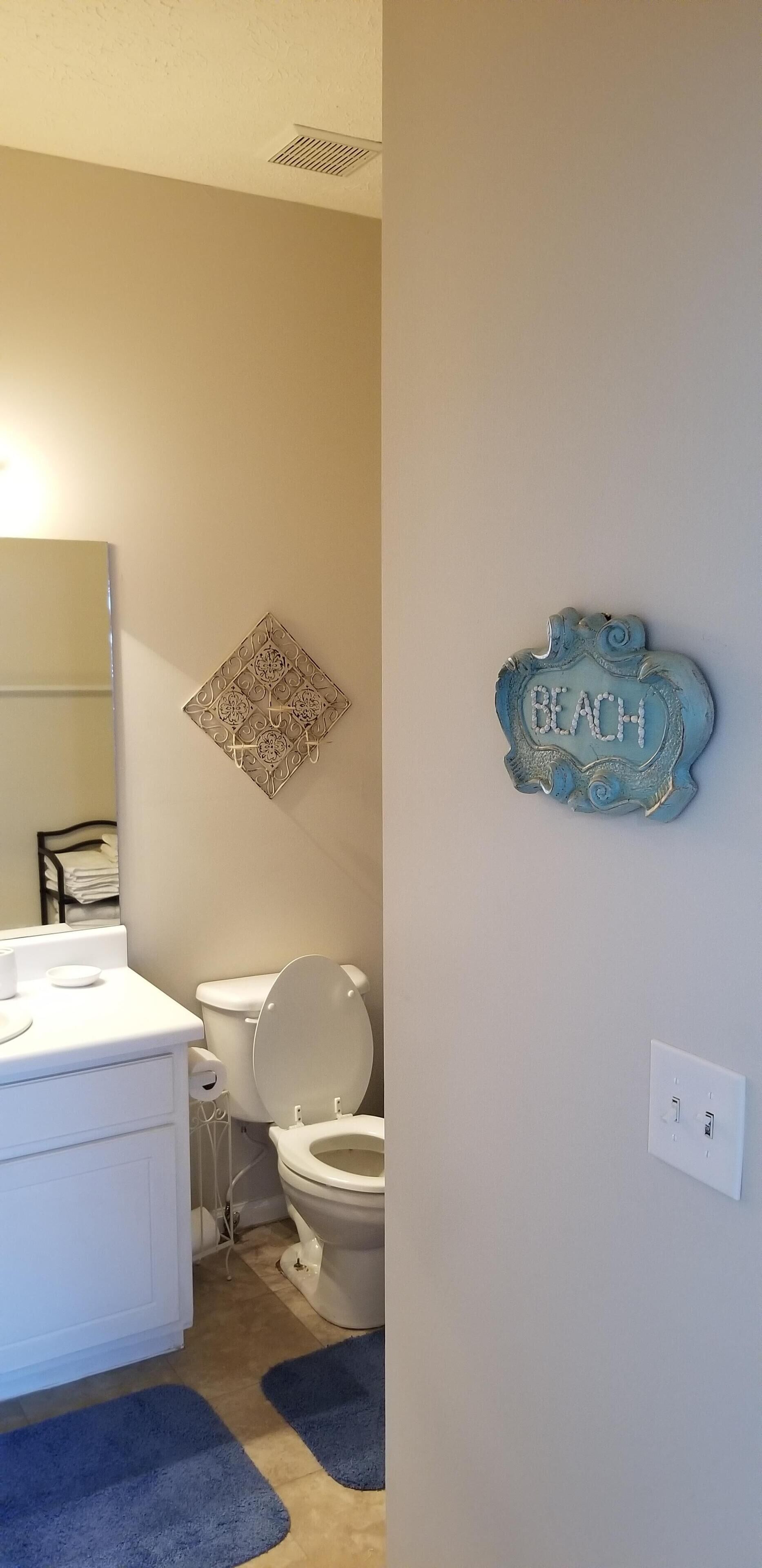 Ein Badezimmer mit Toilette, Waschbecken und einer Wanddekoration mit der Aufschrift 'BEACH'.
