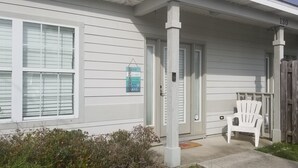 A white house with a porch, a wooden fence, and a white chair outside.