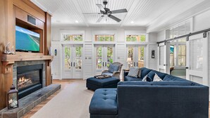 Ein großzügiges Wohnzimmer mit Kamin, Deckenventilator und einem großen Fernseher.