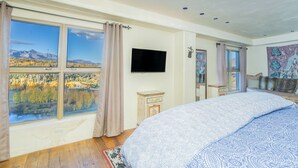 Ein Schlafzimmer mit einem großen Bett, einem Fernseher und Blick auf Herbstlaub durch die Fenster.