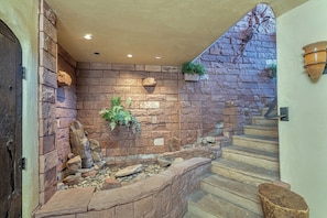 A stone-walled interior with a built-in fireplace, steps leading up to a door, and a hanging planter.