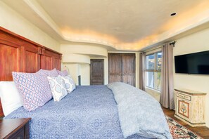A bedroom with a large bed, wooden headboard, and a view of the outdoors through a window.