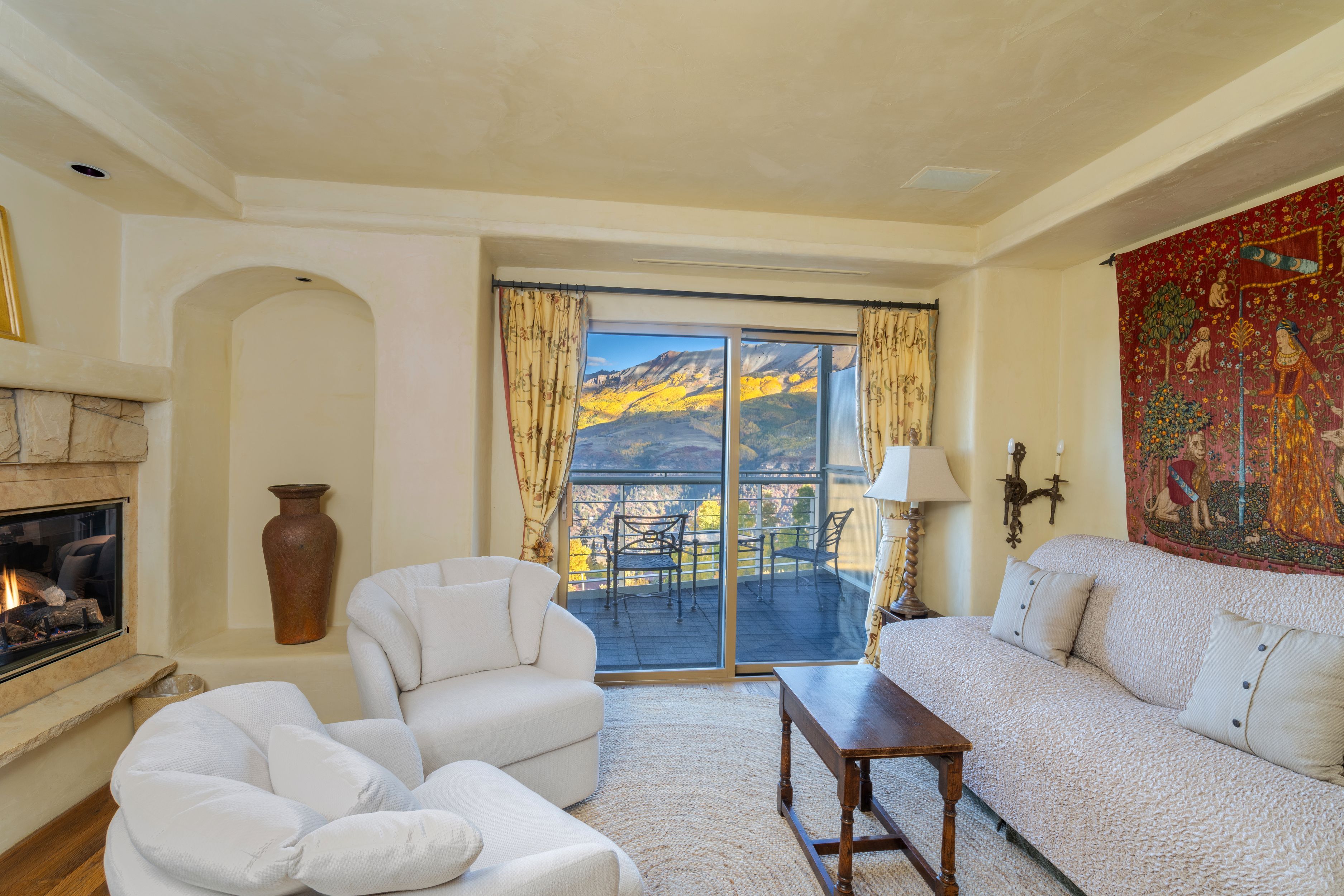 A living room with a fireplace, a sofa, a chair, and a view of mountains through a large window.