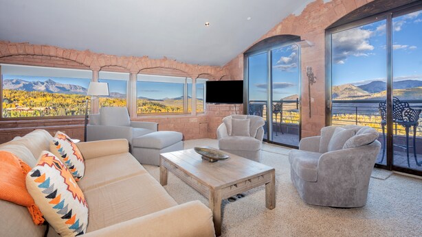 Ein modernes Wohnzimmer mit großem Fenster, Flachbildfernseher und Bergblick.