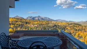 Ein Balkon mit Tisch und Stühlen mit Blick auf eine gebirgige Landschaft im Herbstlaub.